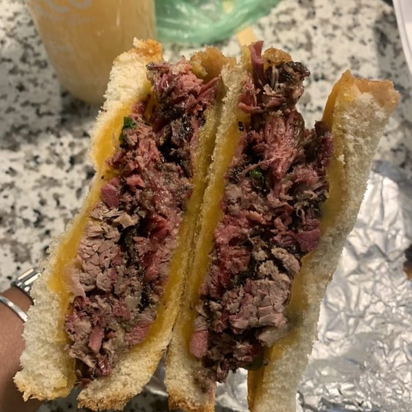 A Smith Spot BBQ brisket sandwich, cut in half, revealing juicy meat and melted cheese on toasted bread.