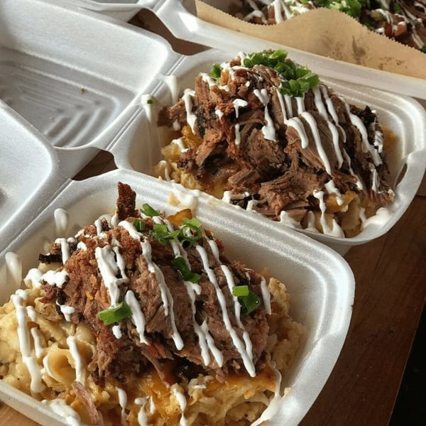 Two Smith Spot BBQ mac and cheese bowls topped with pulled pork, white sauce, and green onions.