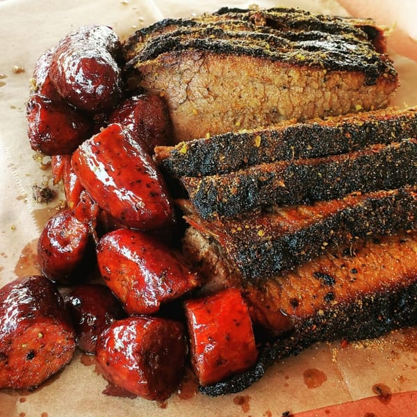 Smith Spot BBQ's sliced brisket with a dark crust and glazed red sausages on butcher paper.