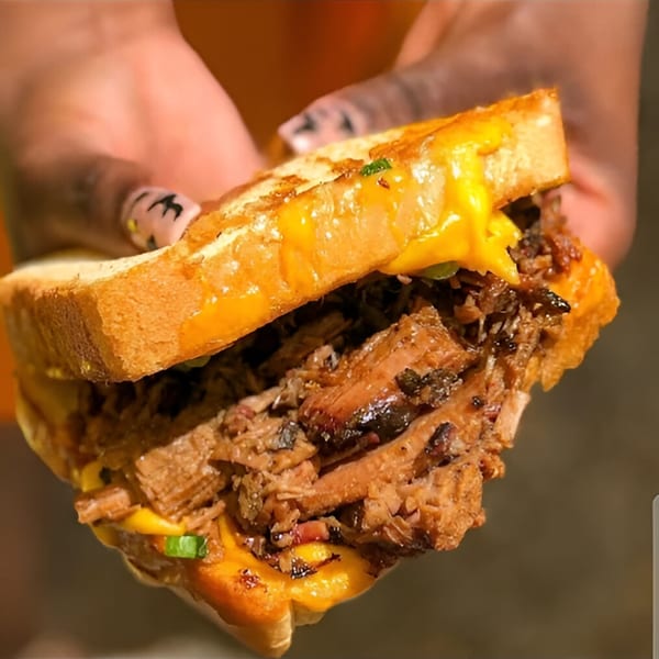 Hands holding a Smith Spot BBQ brisket sandwich with melted cheese and green onions.